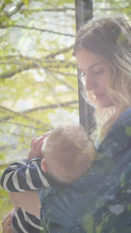 animation of trees in sunshine over caucasian mother with baby drinking milk