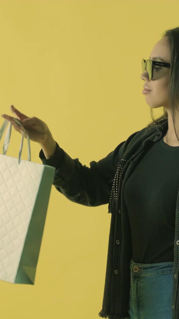 Giovane donna elegante con una borsa della spesa su sfondo giallo