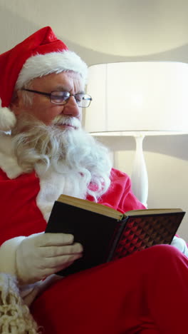 santa claus mirando por la ventana mientras lee una novela