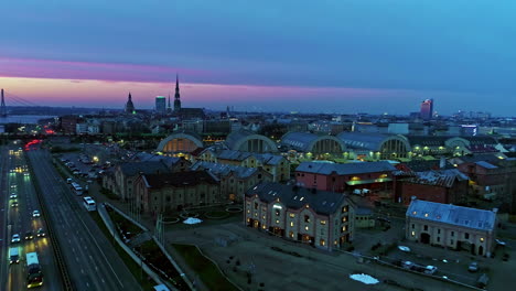 Toma-Aérea-De-Torres-A-Lo-Largo-Del-Horizonte-De-La-Ciudad-De-Riga-Durante-La-Puesta-De-Sol-Con-Cielo-Púrpura-Y-Azul-Sobre-El-Horizonte