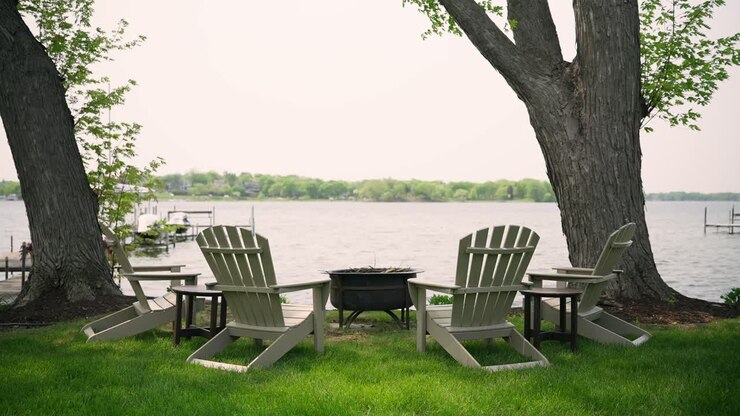 Sedie Adirondack attorno a un focolare in riva a un lago calmo