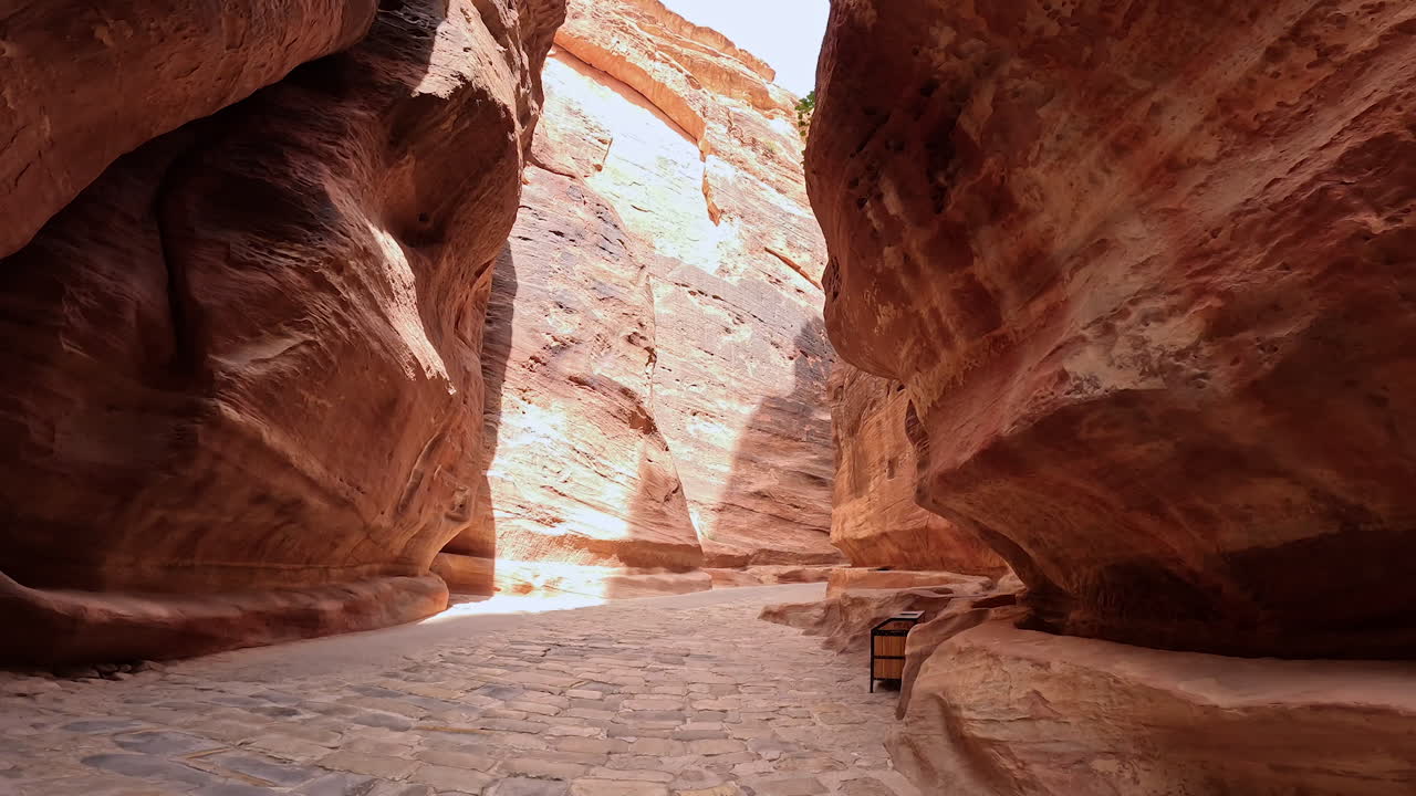 Ancient paved road among the sandstone rocks. Low angle view at the air-cut Al Siq Canyon in Petra, Southern Jordan, West Asia.