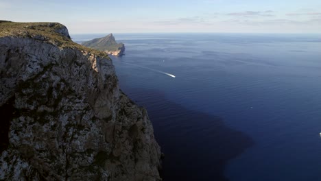 Flying-Around-Corner-Of-Mountain-Reveal-Second-Island-And-Boat,Cala-De-Ses-Ortigues-Mallorca,-Spain,-Aerial