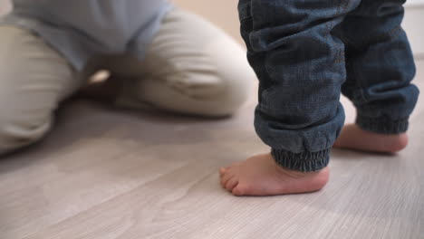 The-Camera-Focuses-On-The-Bare-Feet-Of-A-Baby-Taking-His-First-Steps-Towards-His-Mother