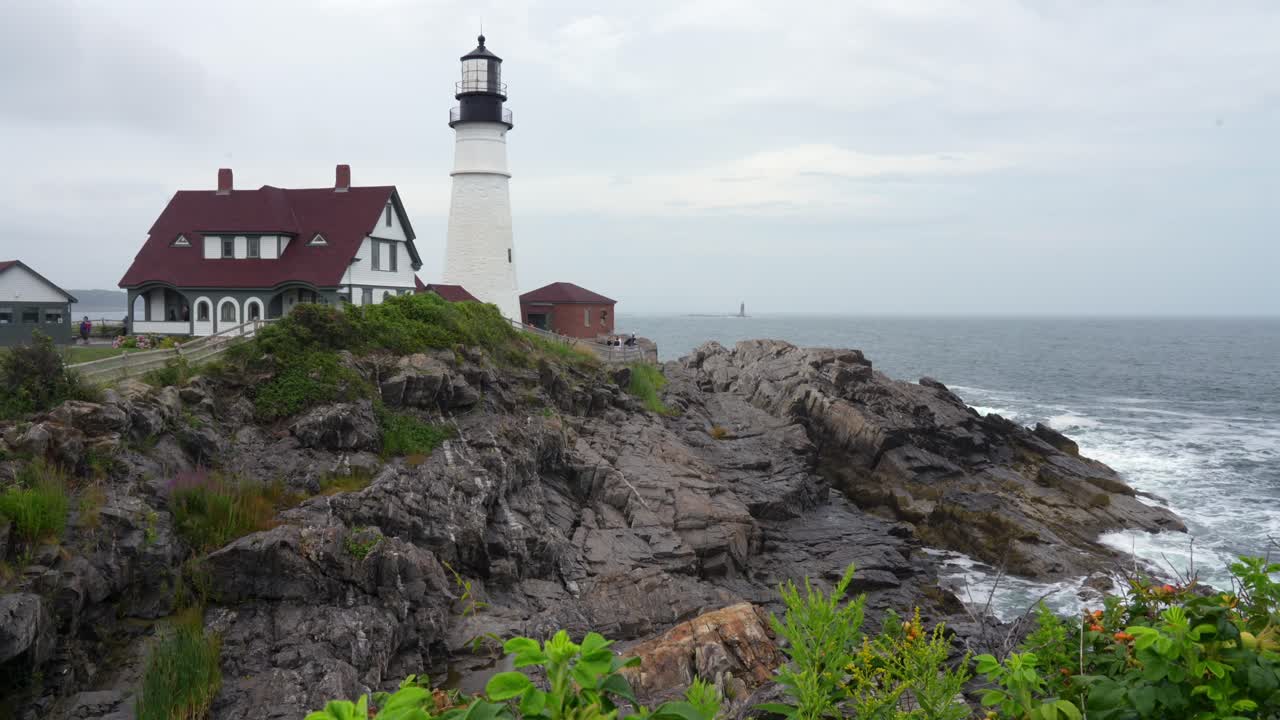 A view of the Portland Head Lighthouse and the waves on the rocky shore on a beautiful sunny day in Maine.
