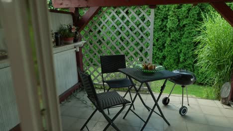 dolly out shot of a terrace in the windy summer with garden table and chairs and a bowl of apples and grill