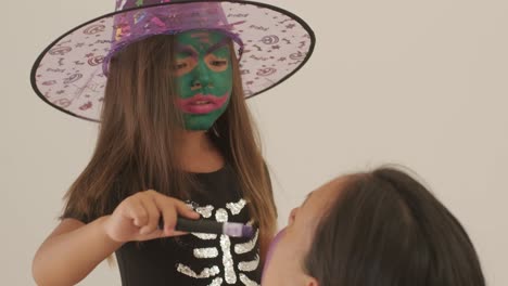 little girl in witch hat applying makeup on pregnant mother for halloween