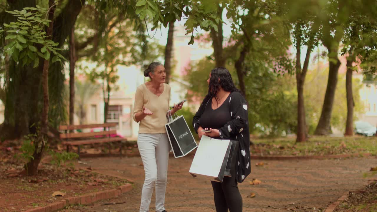 Two women talking and walking in a park with shopping bags