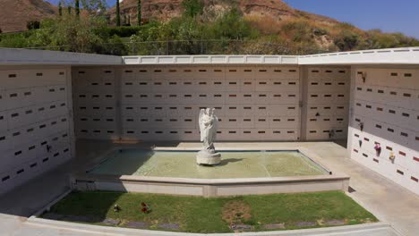 reverse pullback close-up aerial shot of a catholic angel statue in front of a stone mausoleum at a california mortuary