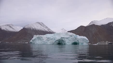 Massive-Iceberg-in-Fjord-by-Coast-and-Snow-Capped-Hills-of-Svalbard,-Norway