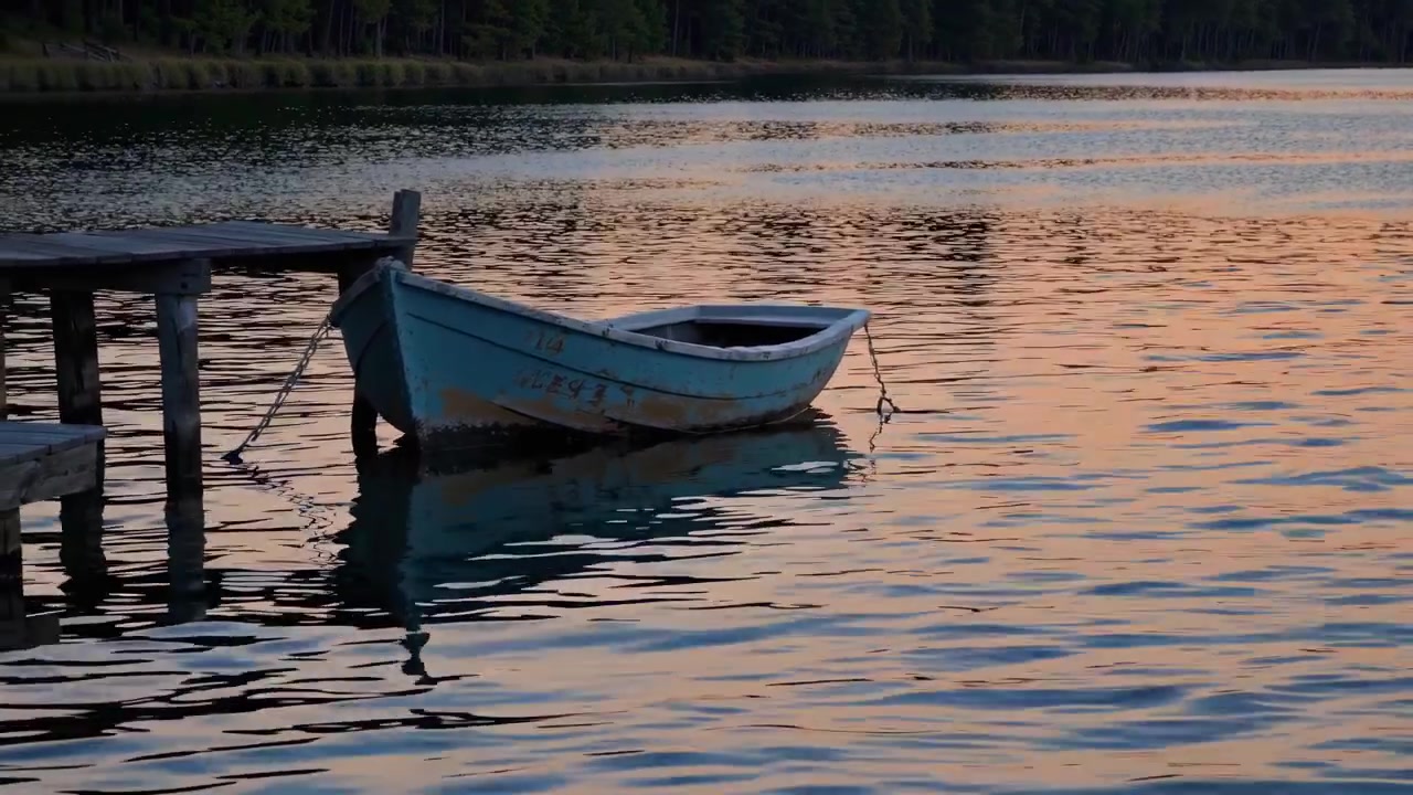 Vecchia barca a remi blu ormeggiata a un molo di legno su un lago al tramonto
