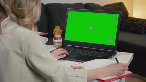 mujer toma notas en el cuaderno de la computadora portátil con pantalla verde.