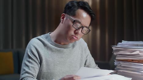 close up of asian man throwing paper and having headache while working hard with documents at home