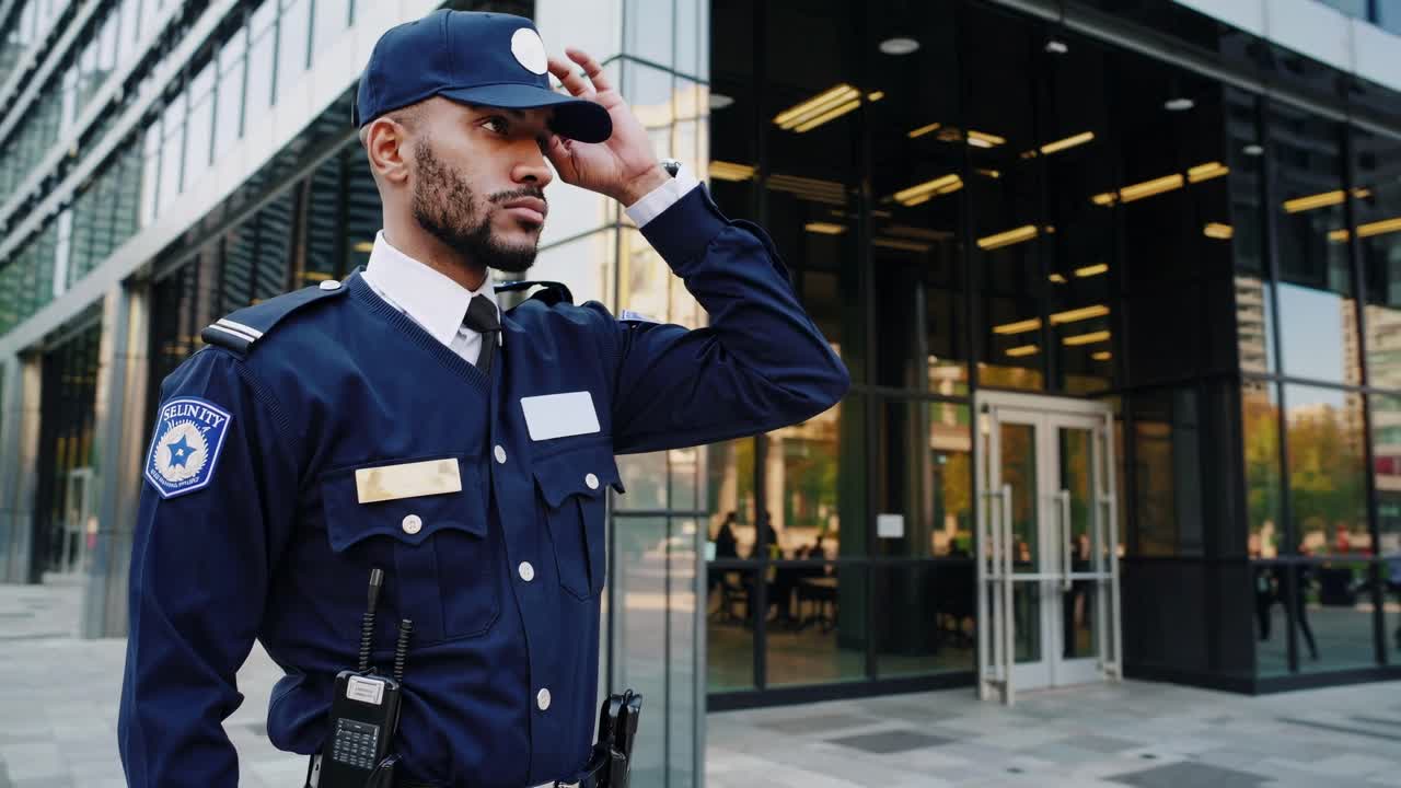 Low-angle video of a security guard adjusting his cap outside a modern glass building