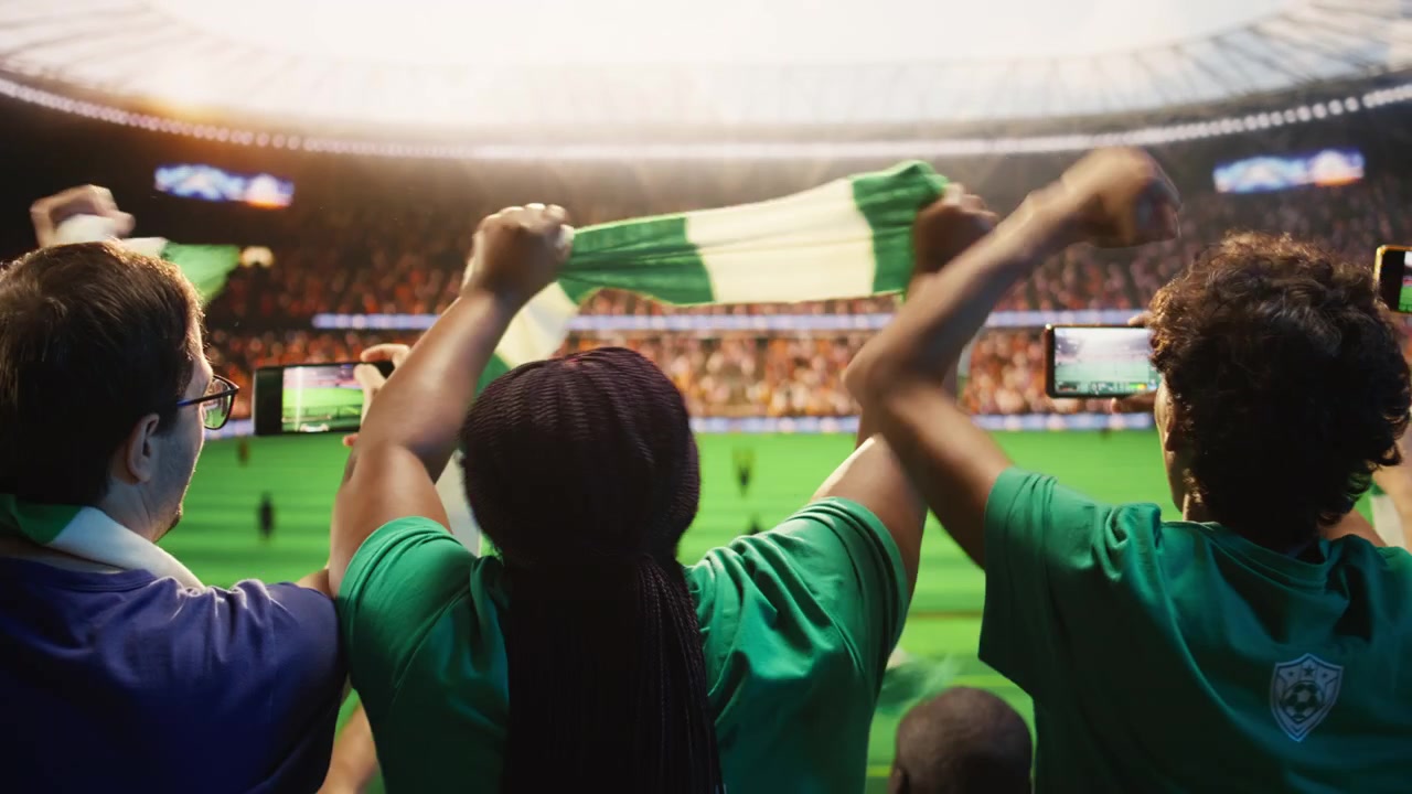 Aficionados al fútbol usando teléfonos inteligentes para grabar un partido jugado en un campo de fútbol