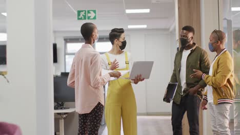 diverse group of male and female business colleagues wearing face masks, working in office
