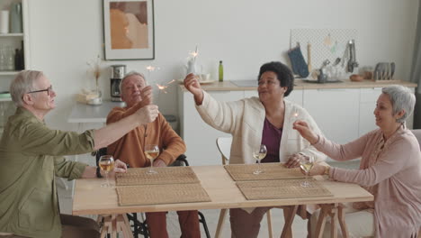medium long of asian and african women, senior handicapped and caucasian men sitting at table in dining room, holding lit bengal lights smiling