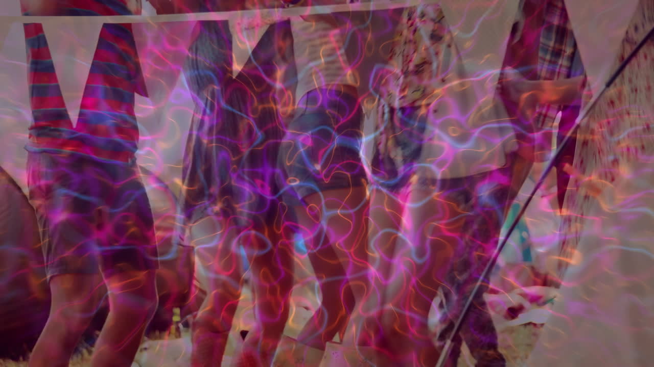 Group of festival attendees dancing on grass at music festival, with neon swirling light projection