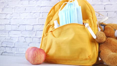 mochila amarilla con máscaras, desinfectante y oso de peluche