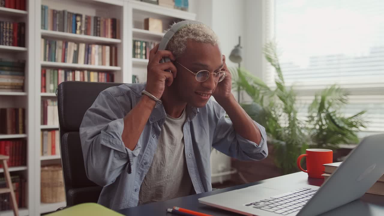 African man opening laptop wearing wireless headphones and starting his workday