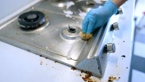 cleaning greasy stovetop. a person wearing gloves scrubs a dirty stovetop with a sponge, removing grease and grime