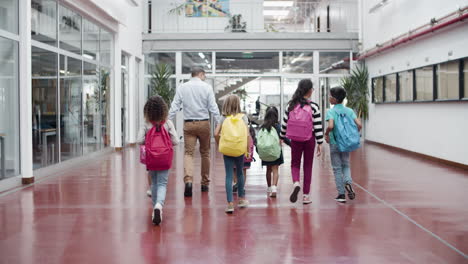 back view of children walking with male tutor in school hallway