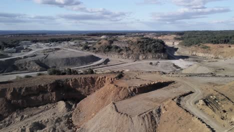 Aerial-curvy-travelling-of-a-hudge-yellow-limestone's-quarry-during-a-beautiful-day-scare-with-the-green-and-wounded-forest