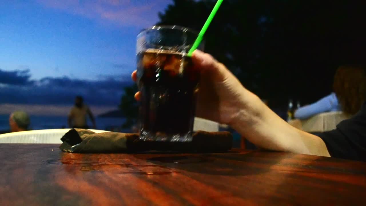 mujer bebiendo de un vaso de cola en la playa en costa rica durante la puesta de sol