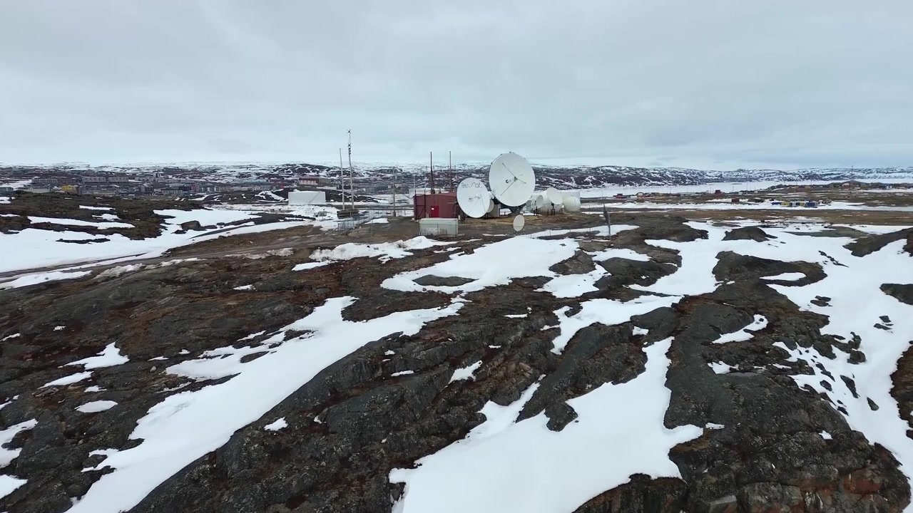 Low-altitude drone approach and reveal of satellite communication dishes on a rocky hill in Iqaluit.