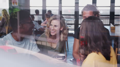 group of friends sitting at table in busy coffee shop talking