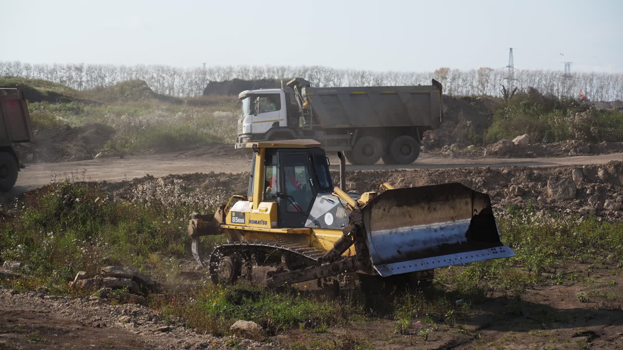 Heavy machinery operating at a construction or industrial site with a bulldozer and dump trucks