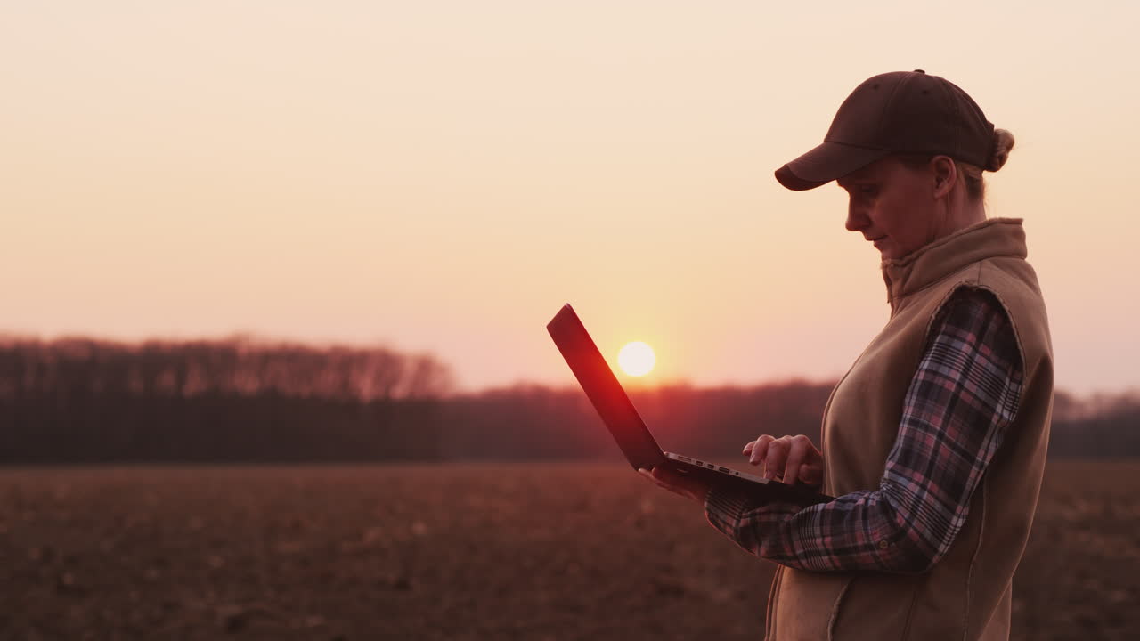 joven agricultora trabaja con una laptop cerca de su campo al atardecer