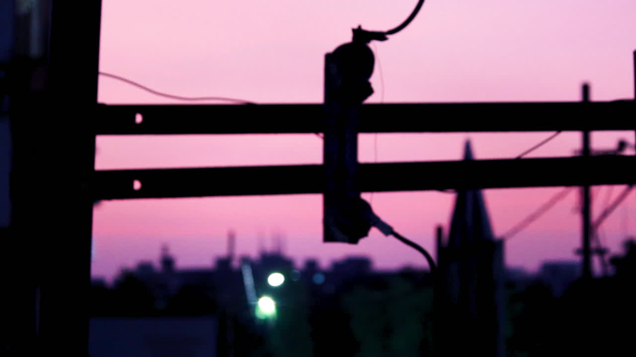 Electric pole silhouette in India with pink dusk sky, showing peaceful evening light and calm urban mood with blurred city background