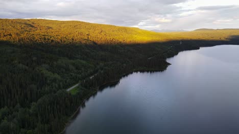 soft, glowing sunlight hitting the forest treeline surrounding dease lake in british columbia, canada