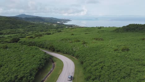 Drone-shot-of-a-car-driving-along-a-winding-forest-road-in-a-tropical-island-during-a-sunny-day