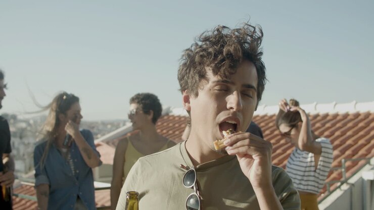 Portrait of a careefree Caucasian man drinking beer and eating pizza while having a rooftop party with friends