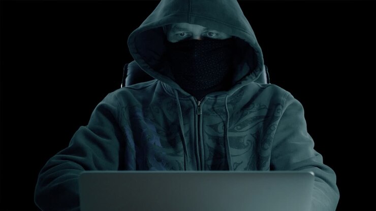 A man in hood sitting at table and coding on laptop. Dark night. Front view close up. Hacker in balaclava mask working at computer. Alpha channel chroma key transparent background.