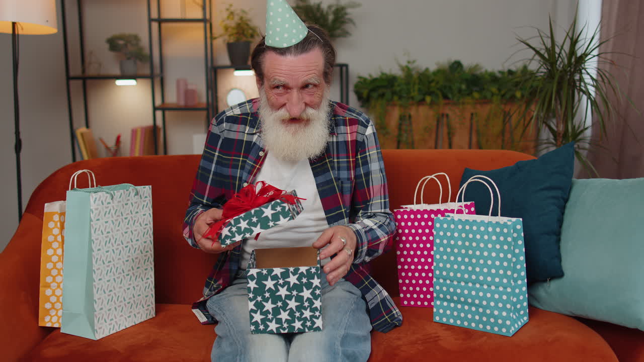 행복 한 노인 은 리본 이 있는 생일 선물 상자 를 들고, 축하 파티 를 열고, 집 에서 선물 을 열고 있다