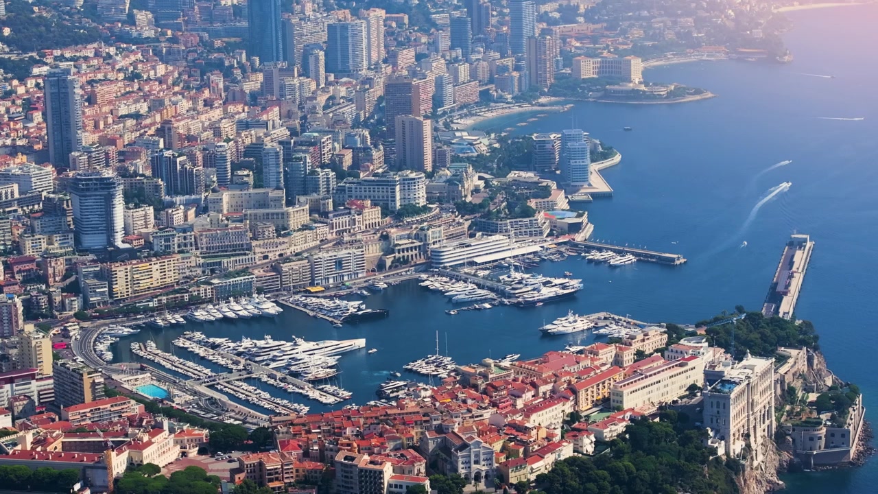 Il porto di Monaco mostra diversi yacht ormeggiati con lo skyline della città sullo sfondo. Grattacieli e imbarcazioni riflettono l'atmosfera vibrante di questa località mediterranea.