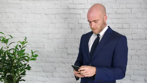 Un-Hombre-De-Negocios-En-Un-Traje-Con-Barba-Enviando-Mensajes-De-Texto-Y-Navegando-En-Su-Teléfono-Mientras-Está-En-Un-Descanso-En-El-Trabajo