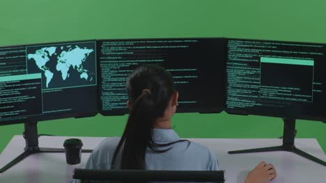 vista trasera de una desarrolladora asiática que tiene dolor de cabeza mientras escribe código con múltiples pantallas de computadora en el estudio de pantalla verde