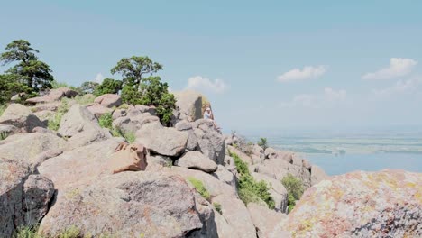 a person sitting on a rocky mountain overlooking a lake and wind turbines