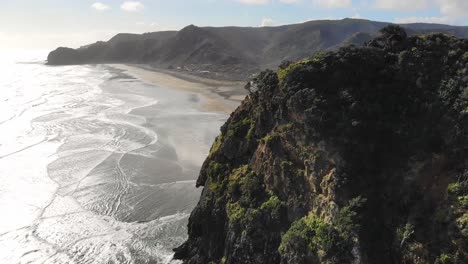 epic drone view of lion rock and piha beach, waitakere ranges regional park