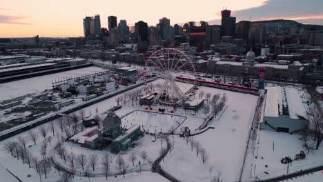 aerial shot over the old port of montreal with the ice skating ring and the ferris wheel in the foreground and the city skyline in the background at sunset in winter, quebec region, canada