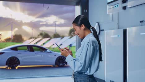 side view of asian female with her smartphone with home energy storage system in a modern garage, checking on her smartphone with meditation