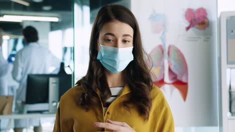 vista de cerca de una paciente caucásica con mascarilla médica sentada en una consulta hospitalaria hablando de su problema de salud con el médico