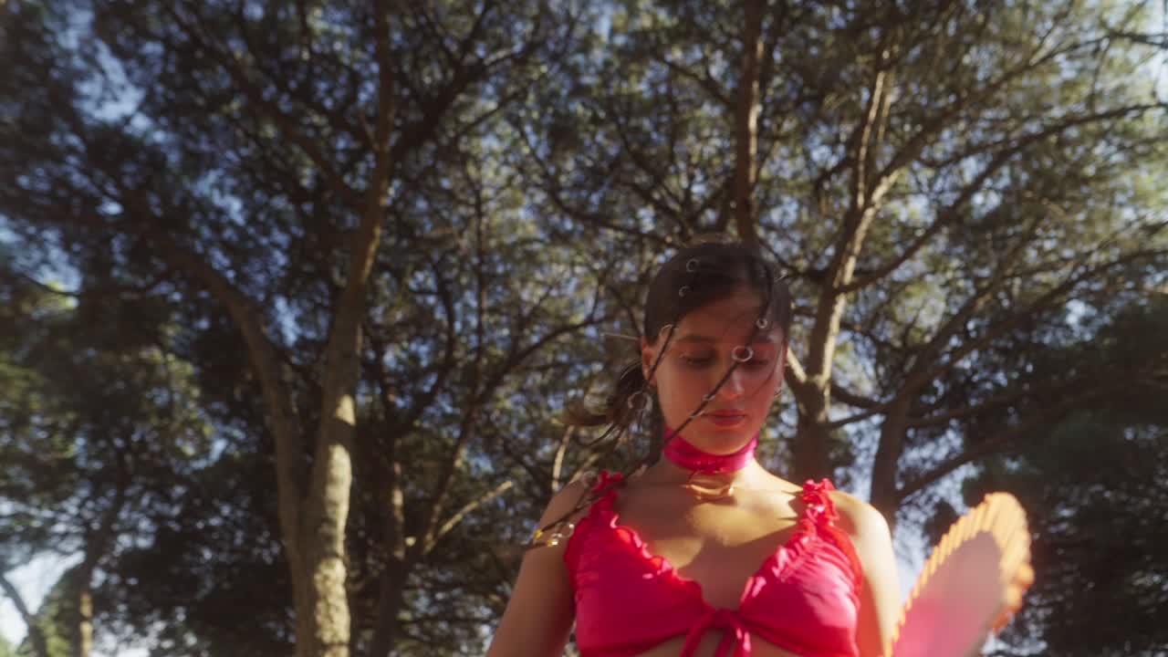 A woman posing with a fan in a sunlit forest