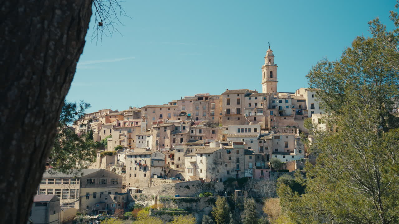 Una vista panoramica di Bocairent, Spagna, rivela case in pietra stratificate e un'imponente torre campanaria che si erge sulla collina, catturando la bellezza storica del villaggio medievale