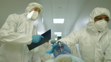 paramedics in protective clothing moving patient through hallway