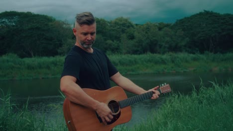 man playing acoustic guitar by a river